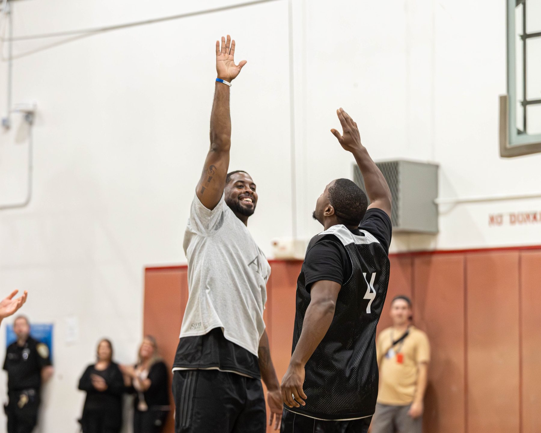 A participant and facilitator raise their hands together during a moment of breakthrough in the gym