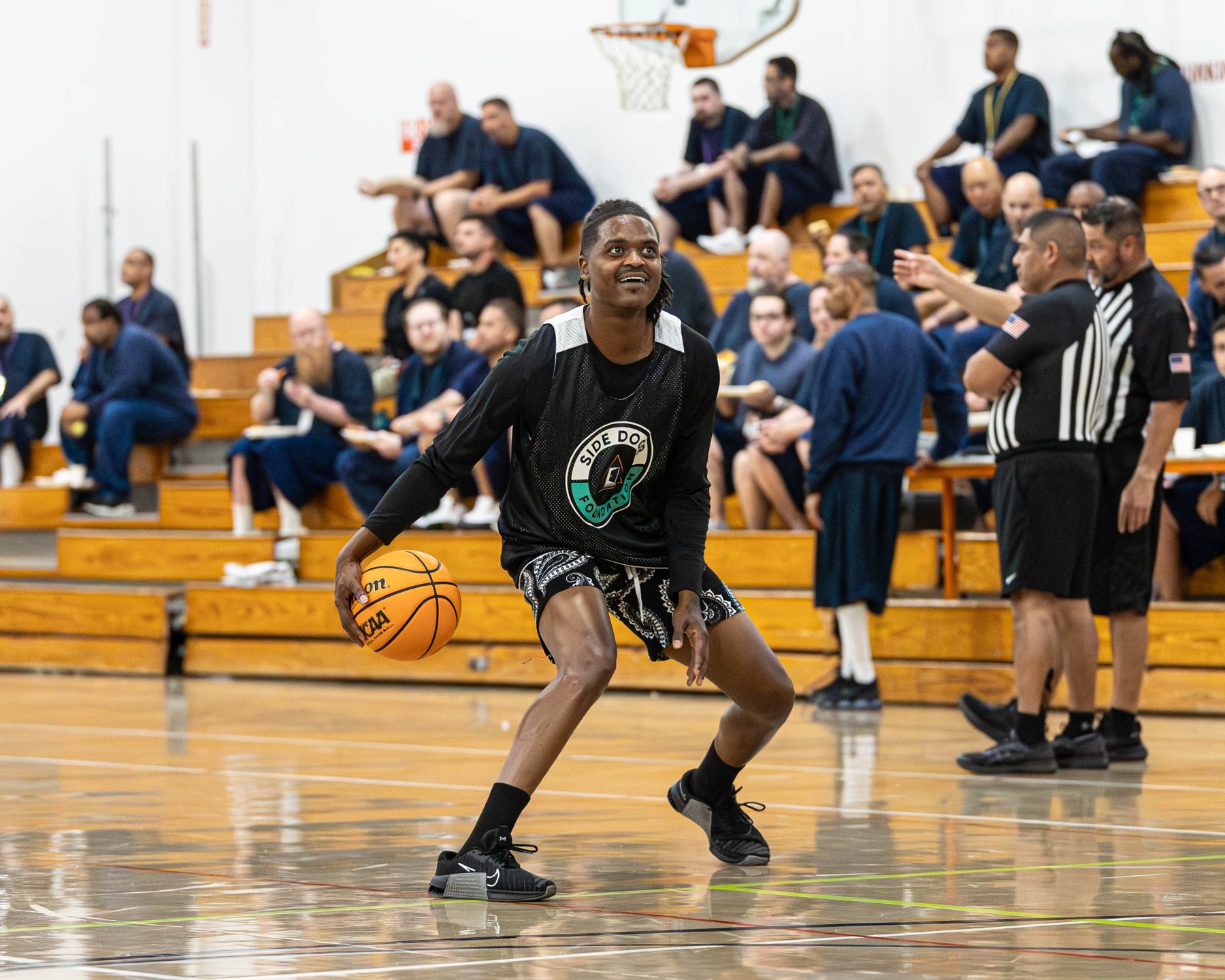 A player drives to the basket inside a correctional facility gym as residents and staff watch